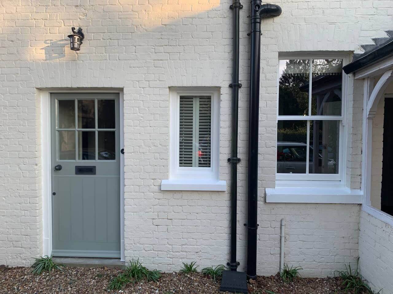 White painted brick cottage with timber windows, internal shutters and a grey front door