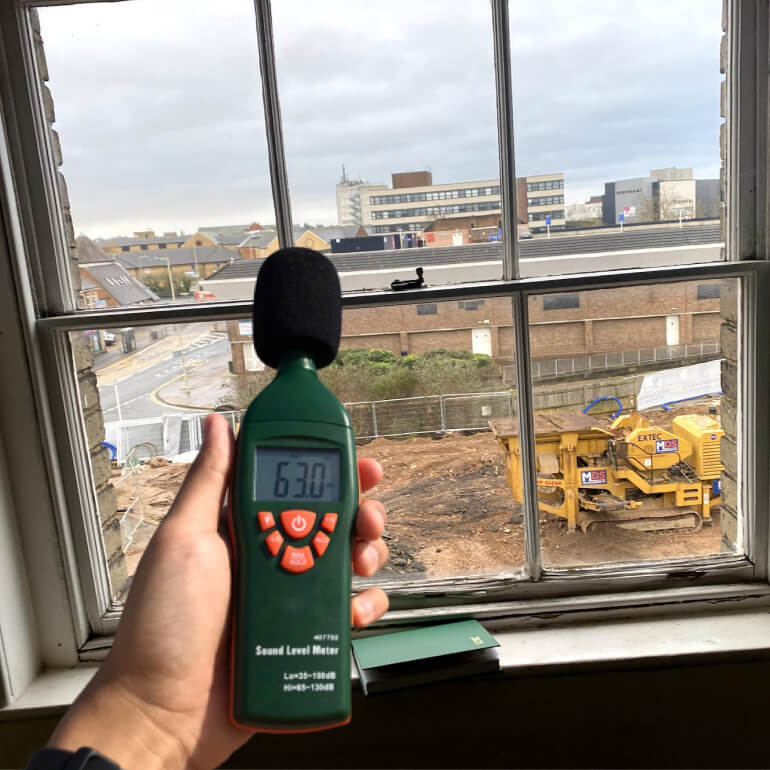 Sound level meter held at an open sash window above a busy street